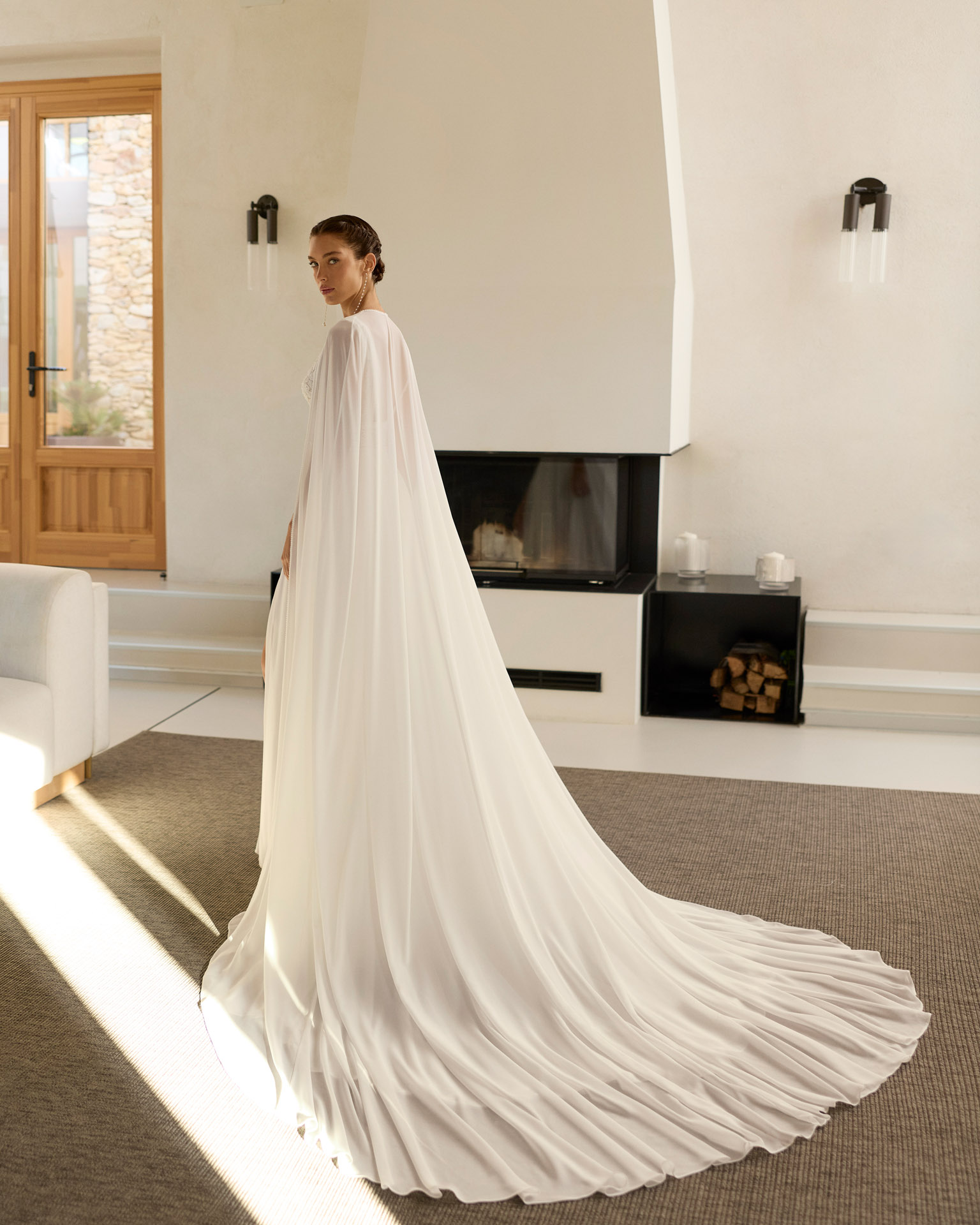 Vestido de novia Raya de Aire Barcelona 2027 de corte A en gasa plisada con escote en pico, cuerpo de encaje floral, espalda abierta y abertura frontal en la falda.