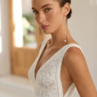 Vestido de novia Raya de Aire Barcelona 2027 de corte A en gasa plisada con escote en pico, cuerpo de encaje floral, espalda abierta y abertura frontal en la falda.