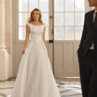 Vestido de novia Bacara de Aire Barcelona 2027 con escote barco, espalda en V, cintura de encaje y falda fluida de crepé.