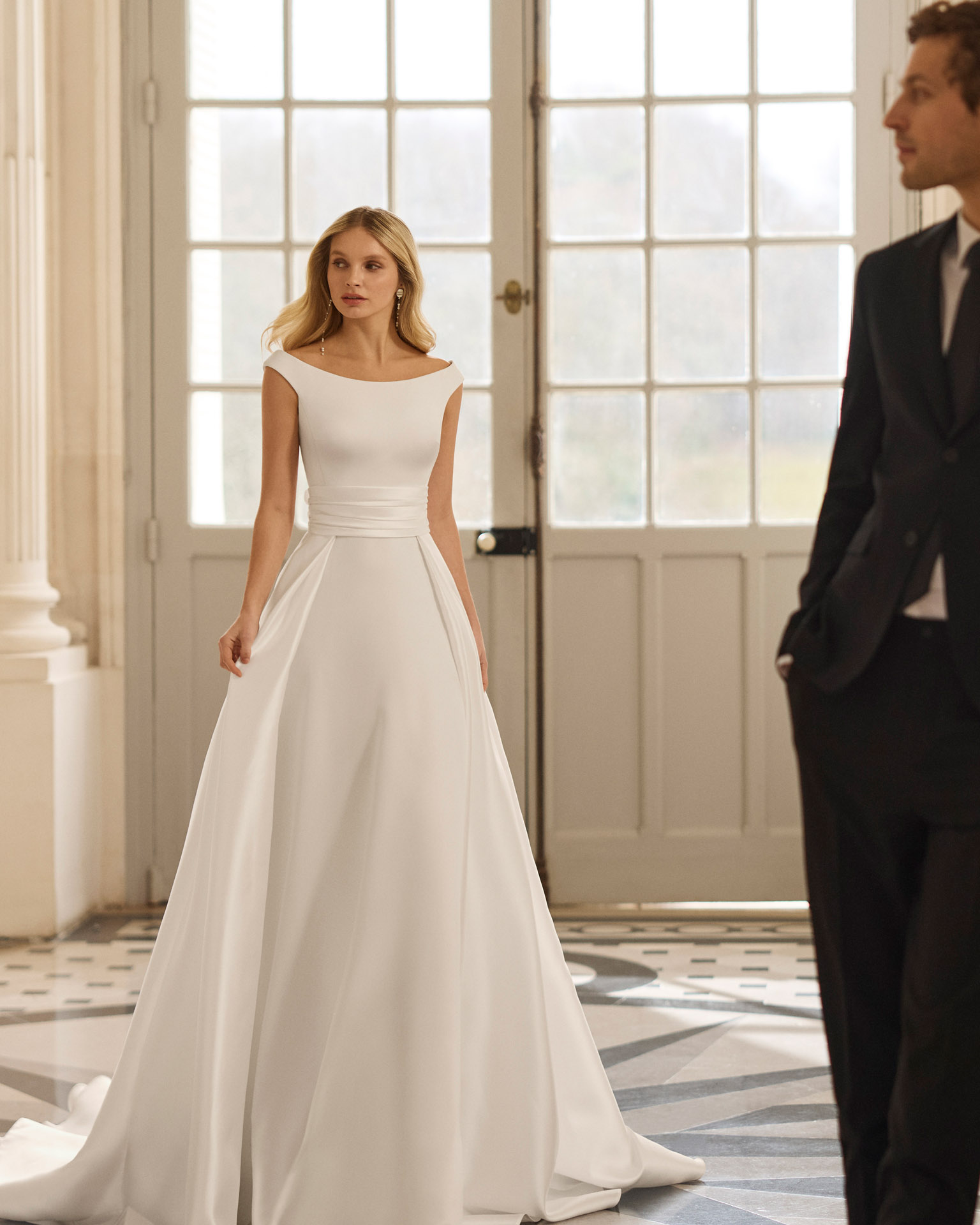 Vestido de novia Bacara de Aire Barcelona 2027 con escote barco, espalda en V, cintura de encaje y falda fluida de crepé.