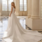 Vestido de novia Bacara de Aire Barcelona 2027 con escote barco, espalda en V, cintura de encaje y falda fluida de crepé.