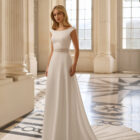 Vestido de novia Bacara de Aire Barcelona 2027 con escote barco, espalda en V, cintura de encaje y falda fluida de crepé.