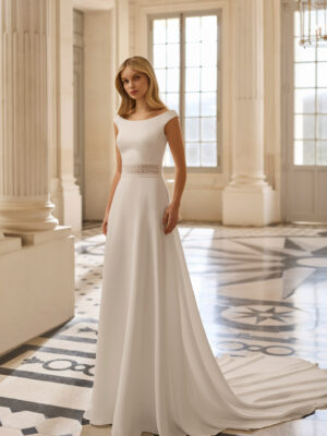 Vestido de novia Bacara de Aire Barcelona 2027 con escote barco, espalda en V, cintura de encaje y falda fluida de crepé.