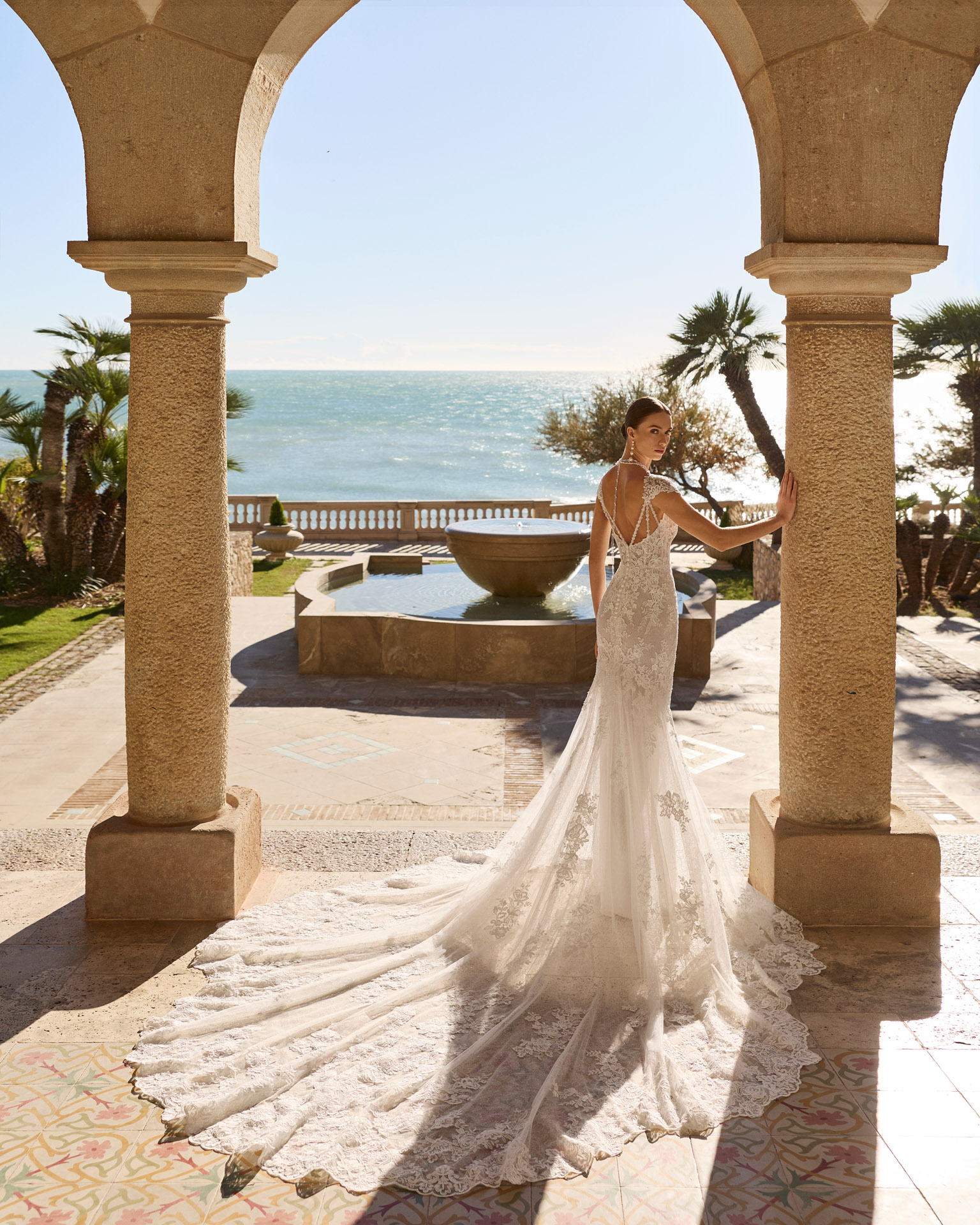 Vestido de novia Fado de Luna Novias 2027 de corte sirena en encaje, escote profundo en V, mangas japonesas de encaje y espalda abierta con delicados tirantes de pedrería.