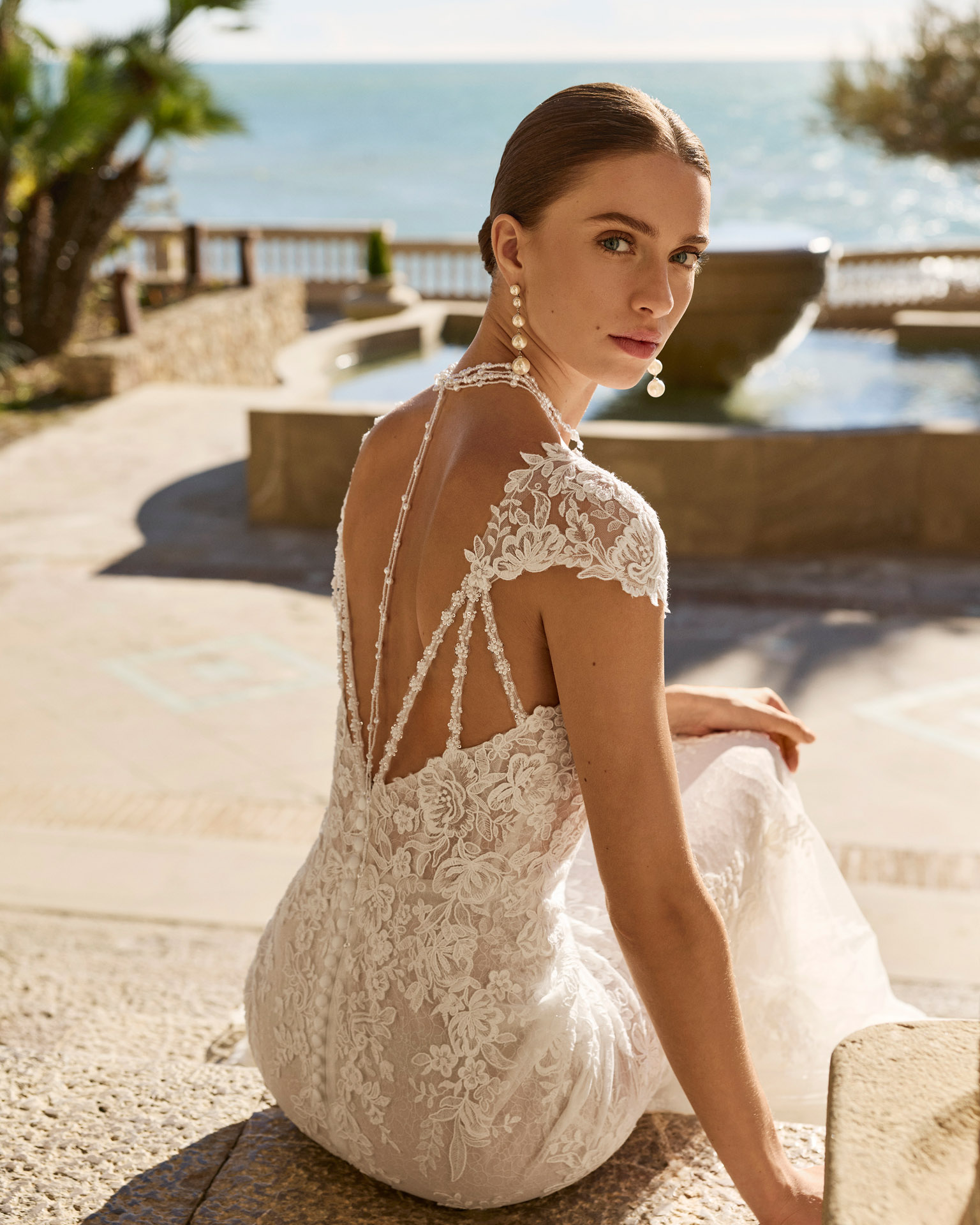 Vestido de novia Fado de Luna Novias 2027 de corte sirena en encaje, escote profundo en V, mangas japonesas de encaje y espalda abierta con delicados tirantes de pedrería.