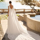Vestido de novia Feliz de Luna Novias 2027 de corte A en gasa con cuerpo de encaje floral, espalda descubierta, delicados detalles de plumas en los hombros y falda fluida.