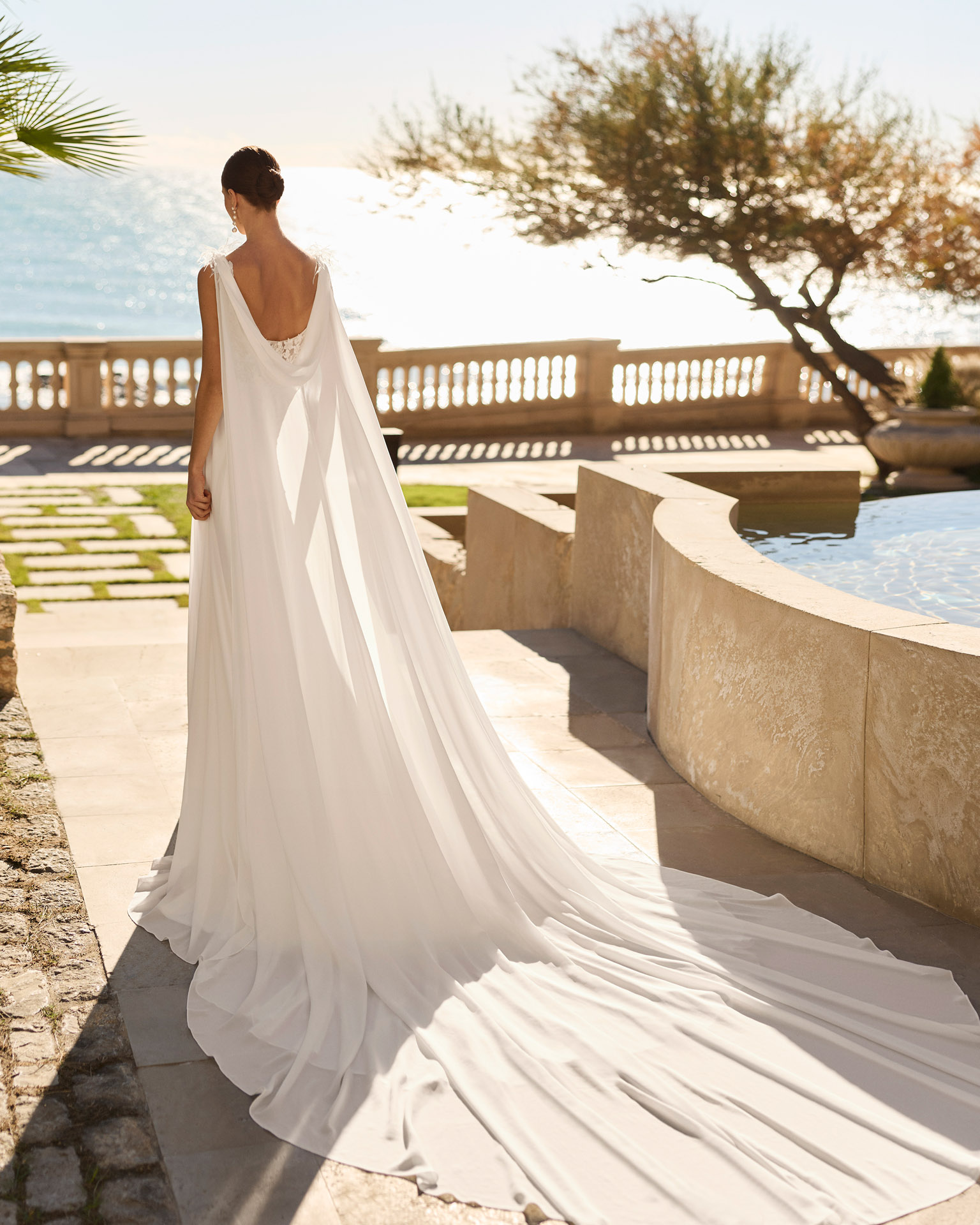 Vestido de novia Feliz de Luna Novias 2027 de corte A en gasa con cuerpo de encaje floral, espalda descubierta, delicados detalles de plumas en los hombros y falda fluida.