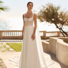 Vestido de novia Feliz de Luna Novias 2027 de corte A en gasa con cuerpo de encaje floral, espalda descubierta, delicados detalles de plumas en los hombros y falda fluida.