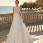 Vestido de novia Fluvia de Luna Novias 2027 de corte princesa, cuello alto y cuerpo de encaje bordado con falda lisa.