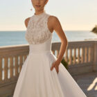 Vestido de novia Fluvia de Luna Novias 2027 de corte princesa, cuello alto y cuerpo de encaje bordado con falda lisa.