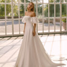 Vestido de novia Frankie de Luna Novias 2027 con escote palabra de honor, mangas abullonadas desmontables, silueta evasé y tejido liso de inspiración minimalista.