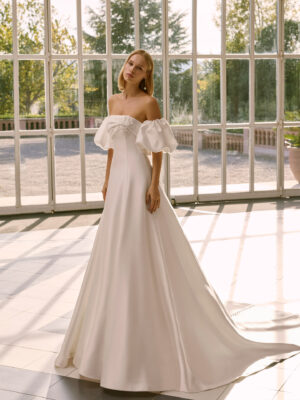 Vestido de novia Frankie de Luna Novias 2027 con escote palabra de honor, mangas abullonadas desmontables, silueta evasé y tejido liso de inspiración minimalista.