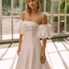 Vestido de novia Frankie de Luna Novias 2027 con escote palabra de honor, mangas abullonadas desmontables, silueta evasé y tejido liso de inspiración minimalista.