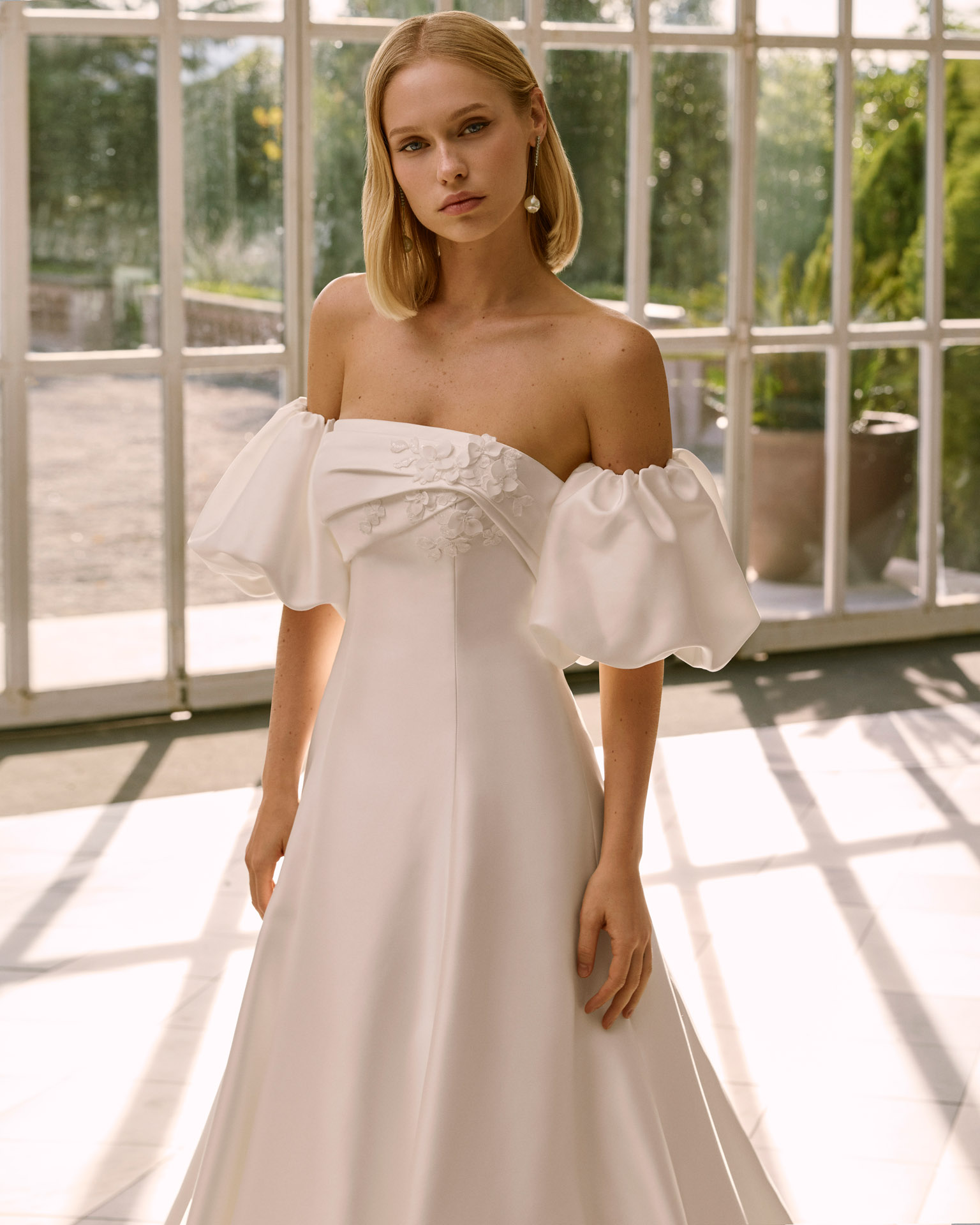 Vestido de novia Frankie de Luna Novias 2027 con escote palabra de honor, mangas abullonadas desmontables, silueta evasé y tejido liso de inspiración minimalista.