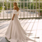 Vestido de novia Frankie de Luna Novias 2027 con escote palabra de honor, mangas abullonadas desmontables, silueta evasé y tejido liso de inspiración minimalista.