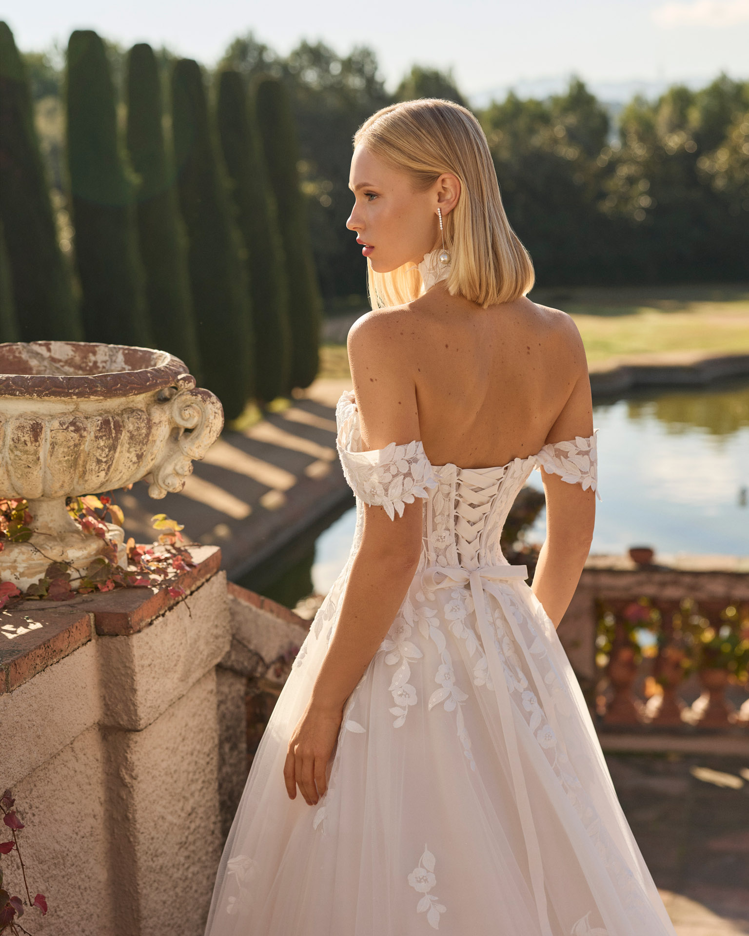 Vestido de novia Fresa de Luna Novias 2027 de corte A con escote barco, mangas caídas de encaje floral, delicado choker de encaje y falda de tul con aplicaciones florales.