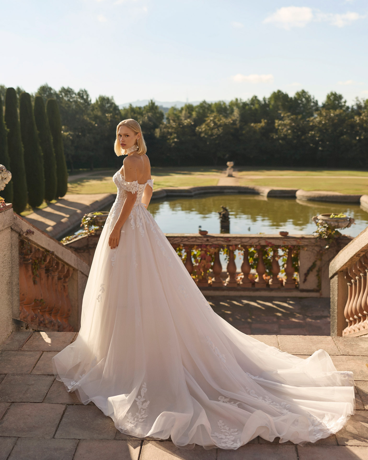 Vestido de novia Fresa de Luna Novias 2027 de corte A con escote barco, mangas caídas de encaje floral, delicado choker de encaje y falda de tul con aplicaciones florales.