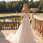 Vestido de novia Fresa de Luna Novias 2027 de corte A con escote barco, mangas caídas de encaje floral, delicado choker de encaje y falda de tul con aplicaciones florales.