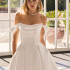 Vestido de novia Fulvia de Luna Novias 2027 de corte princesa, escote barco con hombros descubiertos, cuerpo corsé y falda amplia con cola.