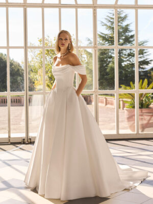 Vestido de novia Fulvia de Luna Novias 2027 de corte princesa, escote barco con hombros descubiertos, cuerpo corsé y falda amplia con cola.
