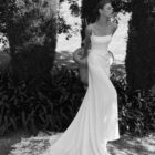 Vestido de novia Marga de Alma Novia 2027 de corte sirena en crepé, escote recto con finos tirantes y espectacular cola de encaje floral.