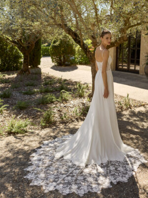 Vestido de novia Marga de Alma Novia 2027 de corte sirena en crepé, escote recto con finos tirantes y espectacular cola de encaje floral.