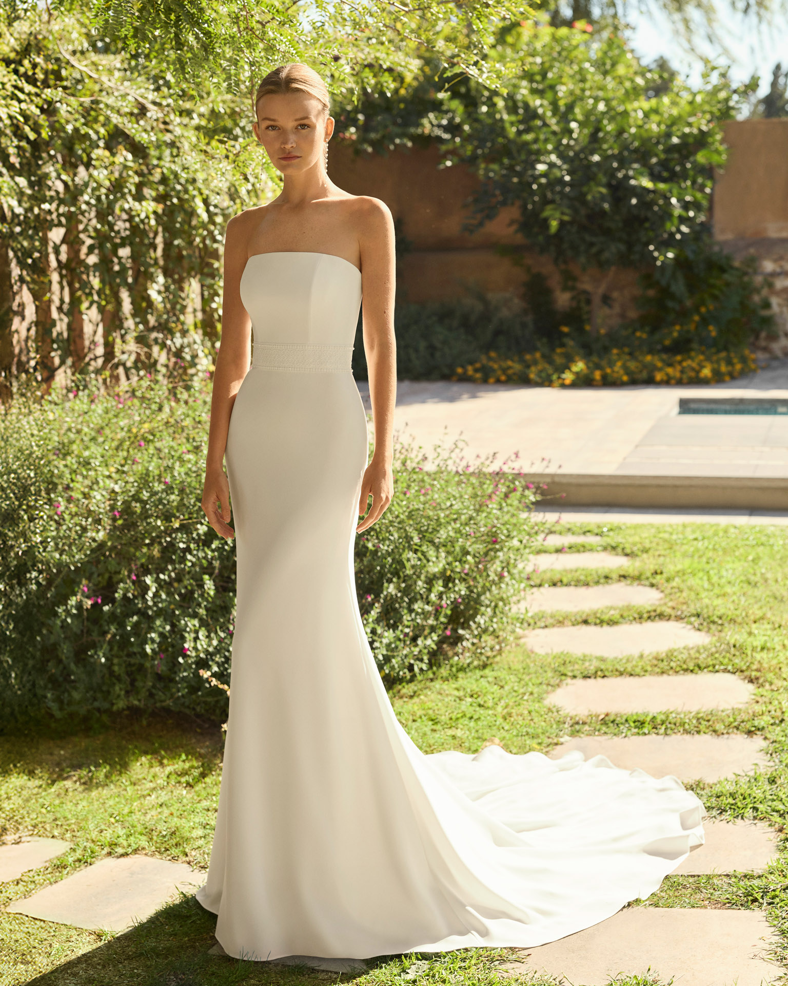 Vestido de novia Megan de Alma Novia 2027 con escote palabra de honor, silueta sirena y chaqueta de encaje desmontable de cuello alto y manga larga.