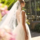 Vestido de novia Milano de Alma Novia 2027 con escote pico, cuerpo de encaje floral, falda de tul con abertura delantera y silueta romántica.