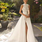 Vestido de novia Mirena de Alma Novia 2027 con vestido corto de encaje floral de cuello alto y elegante sobrefalda desmontable con gran lazada.