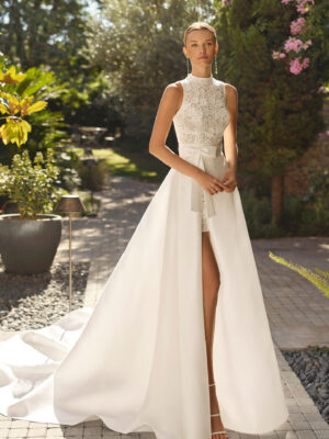 Vestido de novia Mirena de Alma Novia 2027 con vestido corto de encaje floral de cuello alto y elegante sobrefalda desmontable con gran lazada.