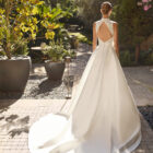 Vestido de novia Mirena de Alma Novia 2027 con vestido corto de encaje floral de cuello alto y elegante sobrefalda desmontable con gran lazada.