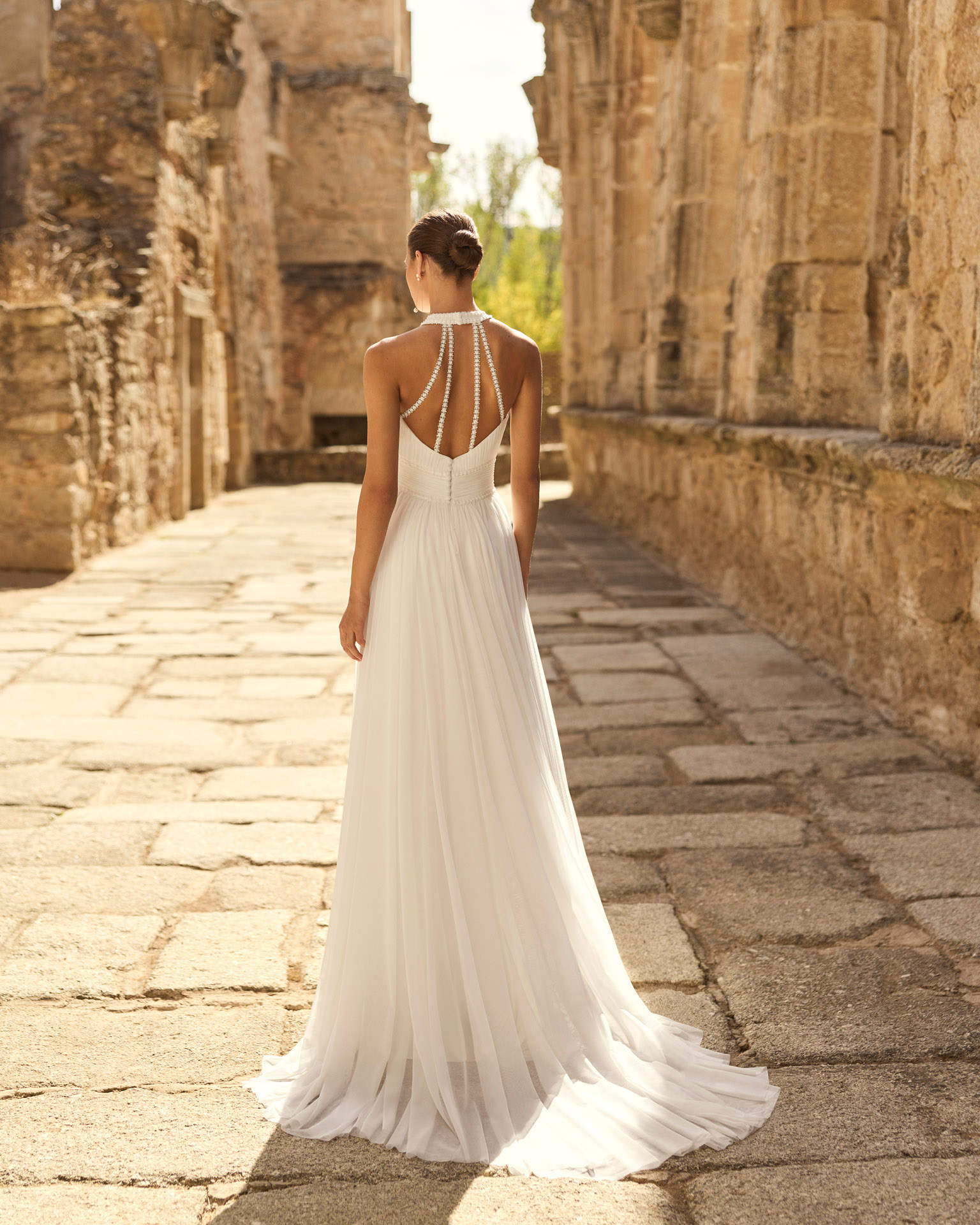 Vestido de novia Palmer de Adriana Alier 2027 con escote halter, falda de gasa plisada, espalda abierta con tirantes joya y estilo romántico.