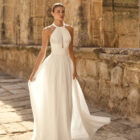 Vestido de novia Palmer de Adriana Alier 2027 con escote halter, falda de gasa plisada, espalda abierta con tirantes joya y estilo romántico.
