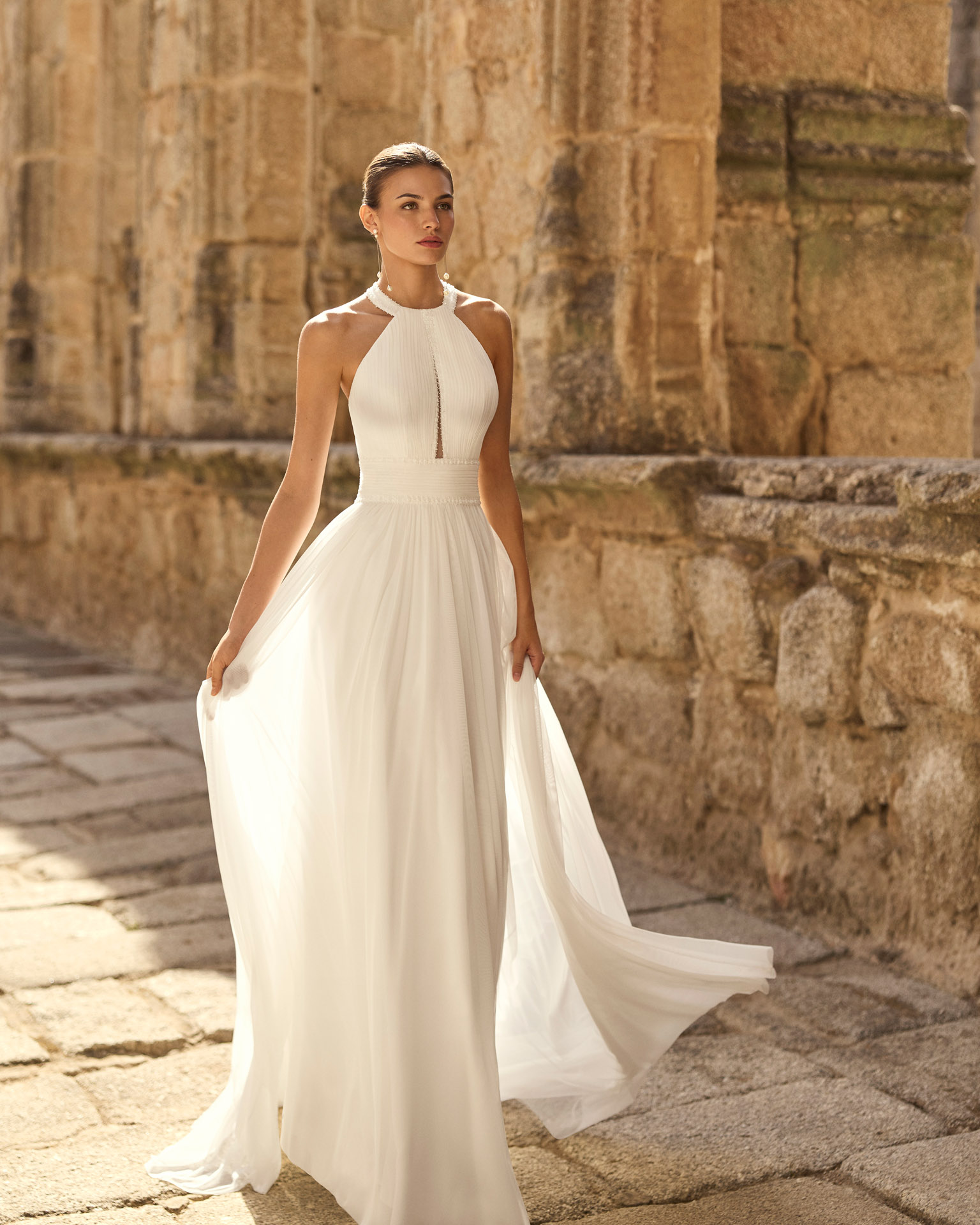 Vestido de novia Palmer de Adriana Alier 2027 con escote halter, falda de gasa plisada, espalda abierta con tirantes joya y estilo romántico.