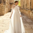 Vestido de novia Palmer de Adriana Alier 2027 con escote halter, falda de gasa plisada, espalda abierta con tirantes joya y estilo romántico.
