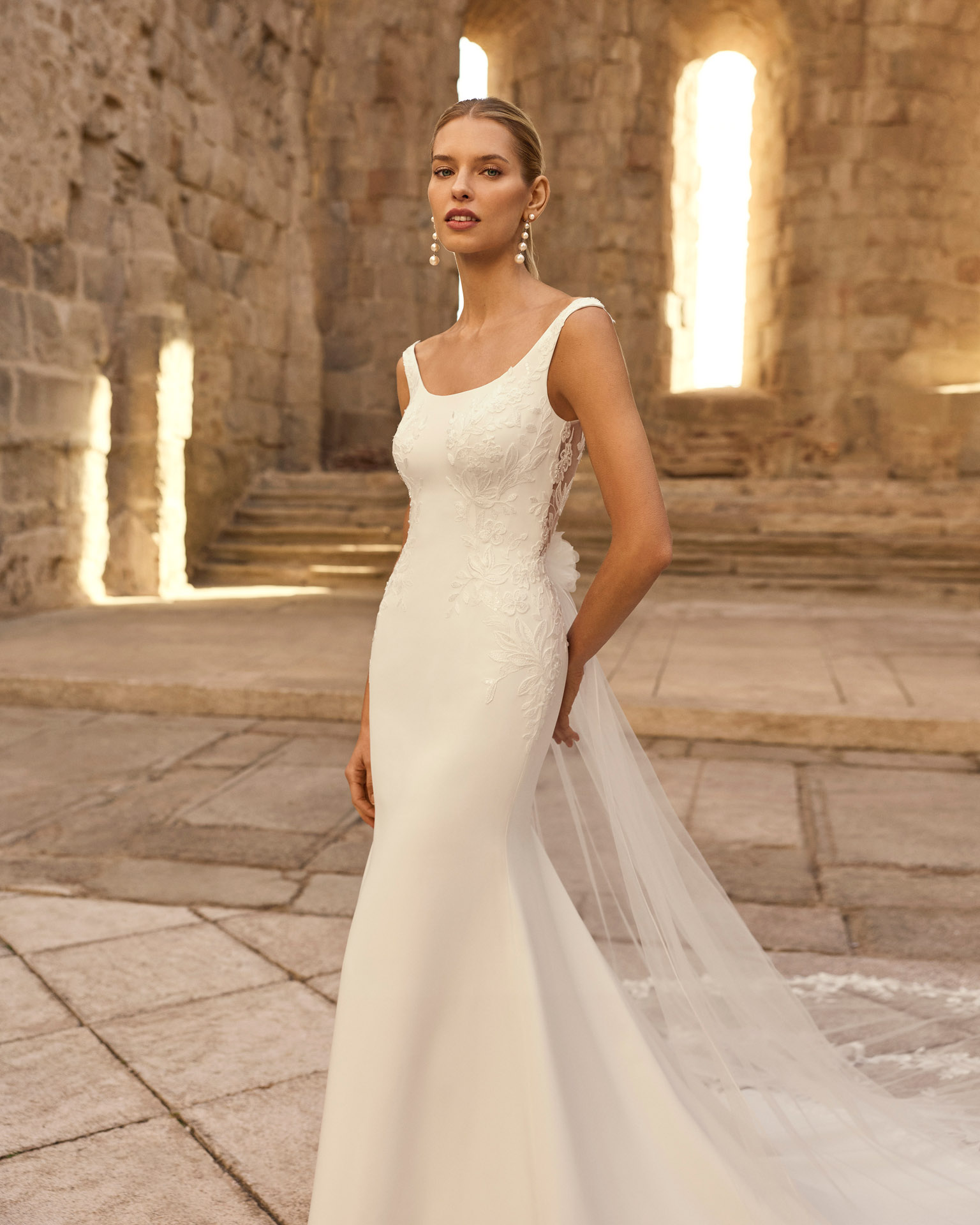 Vestido de novia Parvati de Adriana Alier 2027 de corte sirena en crepé con aplicaciones de encaje floral, escote barco, espalda escotada en V y cola de tul bordada.