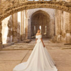 Vestido de novia Piuma de Adriana Alier 2027 con escote barco caído, cuerpo estructurado, gran lazada en la espalda y falda princesa de mikado.