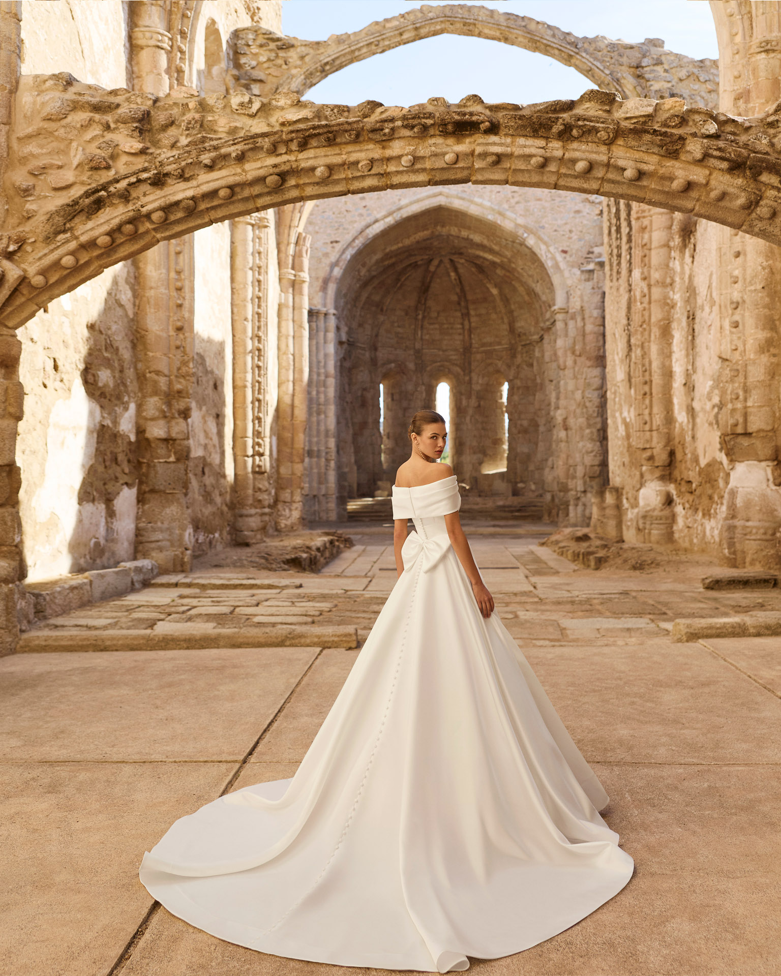 Vestido de novia Piuma de Adriana Alier 2027 con escote barco caído, cuerpo estructurado, gran lazada en la espalda y falda princesa de mikado.