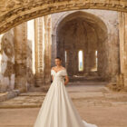 Vestido de novia Piuma de Adriana Alier 2027 con escote barco caído, cuerpo estructurado, gran lazada en la espalda y falda princesa de mikado.