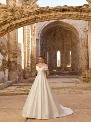 Vestido de novia Piuma de Adriana Alier 2027 con escote barco caído, cuerpo estructurado, gran lazada en la espalda y falda princesa de mikado.