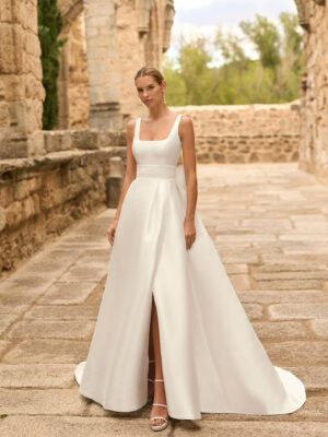 Vestido de novia Porto de Adriana Alier 2027 de línea A con escote cuadrado, abertura frontal, cintura de encaje y sobrefalda desmontable.