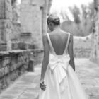 Vestido de novia Porto de Adriana Alier 2027 de línea A con escote cuadrado, abertura frontal, cintura de encaje y sobrefalda desmontable.