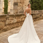 Vestido de novia Prado de Adriana Alier 2027 con cuello halter, espalda completamente descubierta, gran lazo posterior, falda de corte A con abertura lateral y tejido jacquard floral.