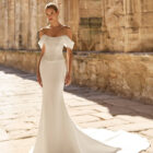 Vestido de novia Pravia de Adriana Alier 2027 de corte sirena en mikado con escote barco, hombros caídos, corsé estructurado y espalda descubierta.