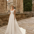 Vestido de novia Prina de Adriana Alier 2027 de línea A con escote barco, cuerpo liso, cintura marcada y falda de gran caída.