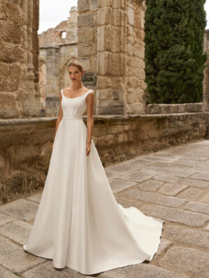 Vestido de novia Prina de Adriana Alier 2027 de línea A con escote barco, cuerpo liso, cintura marcada y falda de gran caída.