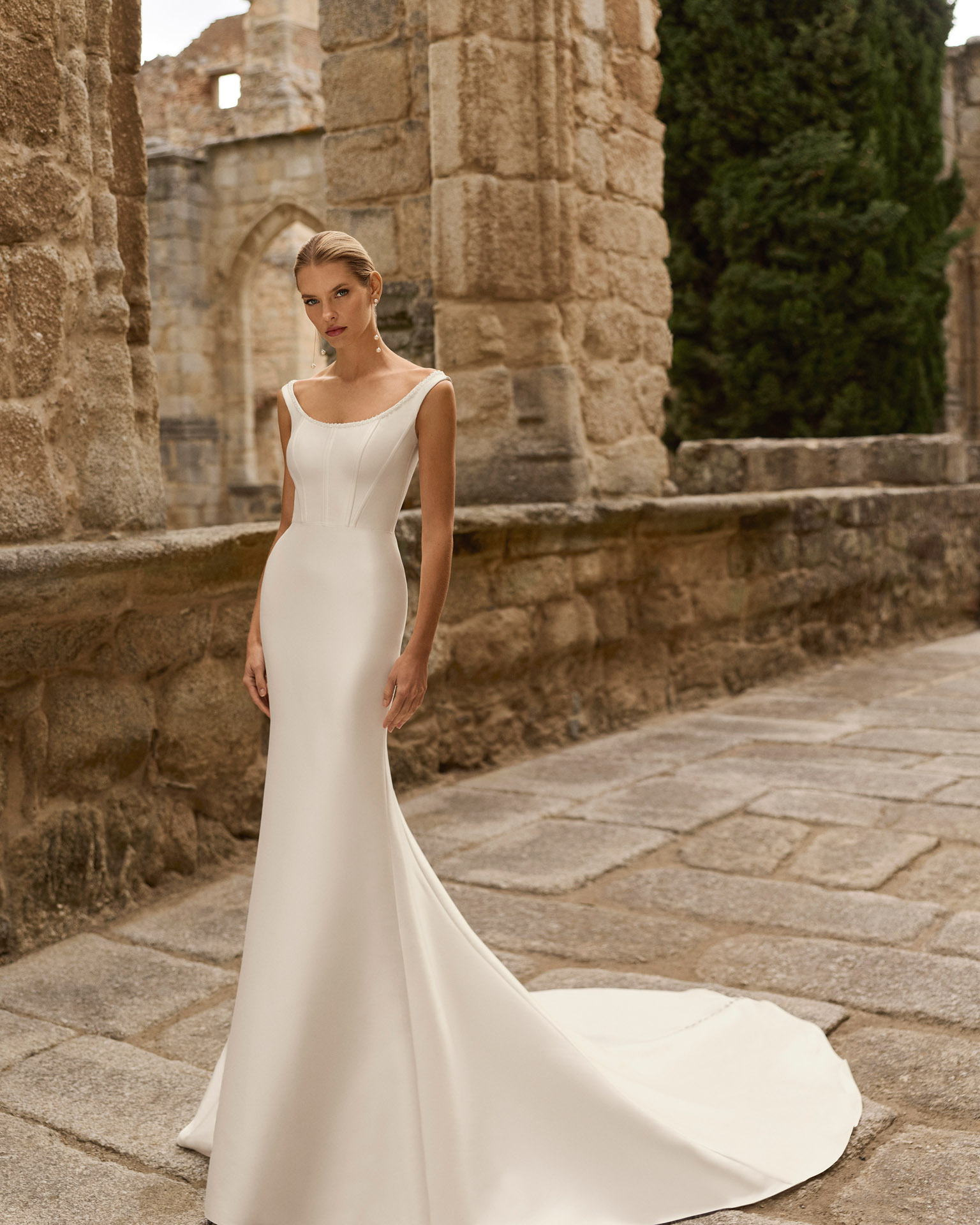 Vestido de novia Prina de Adriana Alier 2027 de línea A con escote barco, cuerpo liso, cintura marcada y falda de gran caída.