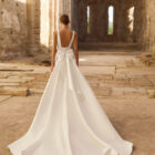 Vestido de novia Princes de Adriana Alier 2027 en crepé con escote en V, mangas largas de gasa, espalda en V con gran lazo y falda de línea A.