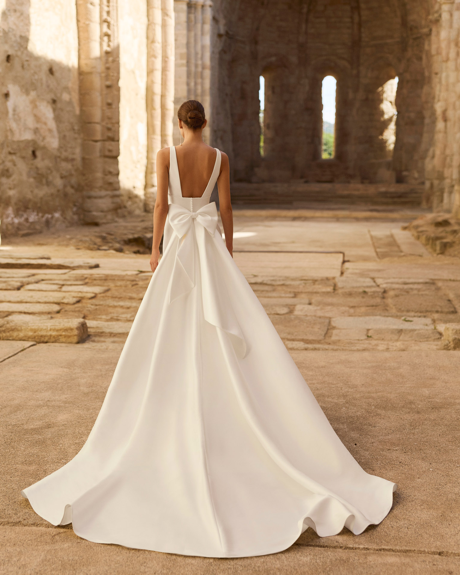 Vestido de novia Princes de Adriana Alier 2027 en crepé con escote en V, mangas largas de gasa, espalda en V con gran lazo y falda de línea A.