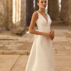 Vestido de novia Princes de Adriana Alier 2027 en crepé con escote en V, mangas largas de gasa, espalda en V con gran lazo y falda de línea A.